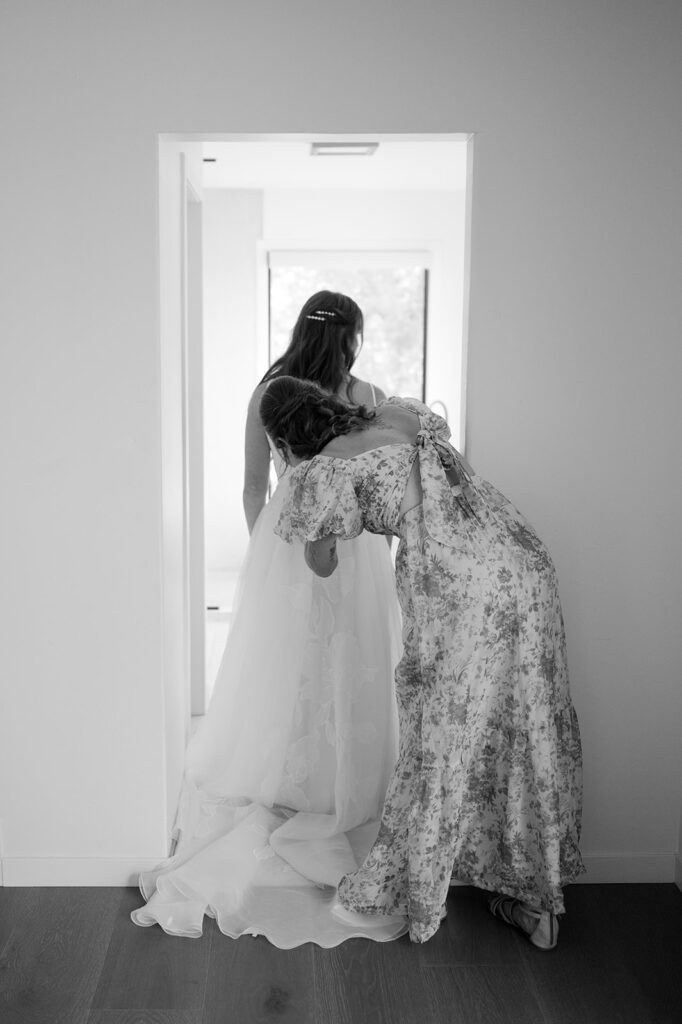 Black and white moment of the bride and her mom zipping up her wedding dress before the ceremony.