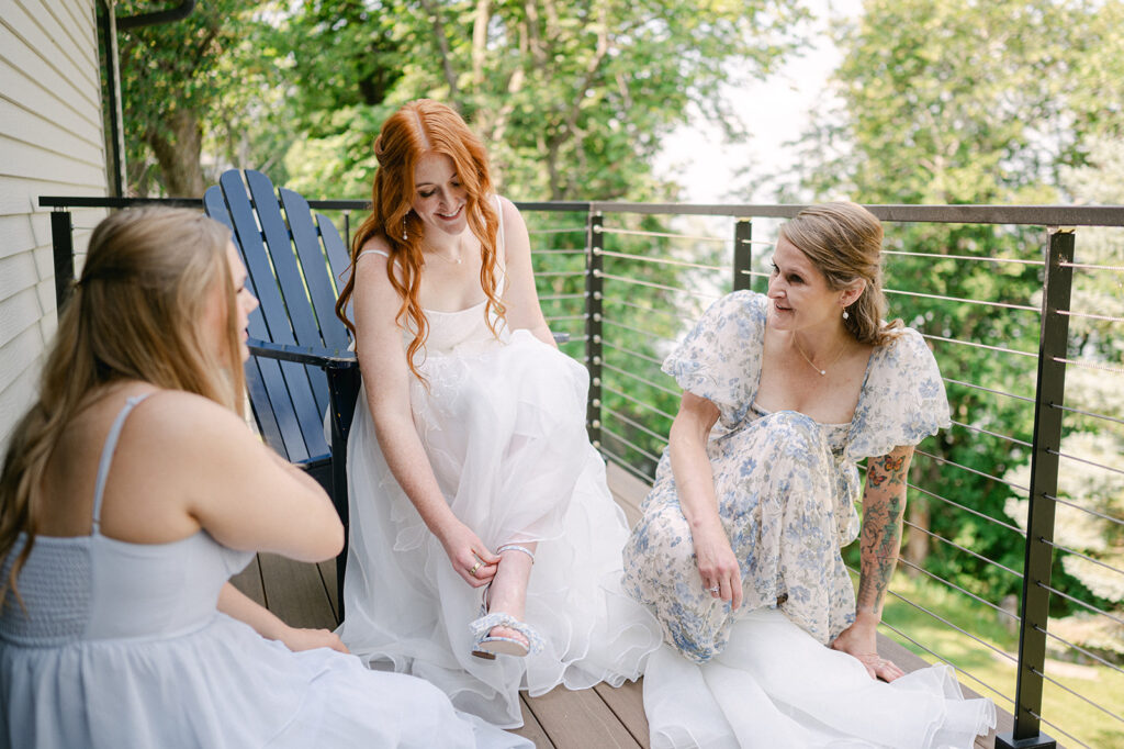 Candid shot of the bride on the porch, putting on her heels with help from her mom and sister.