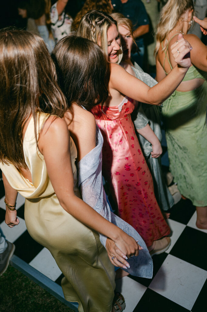 Bridesmaids dancing on a checkered dance floor. 