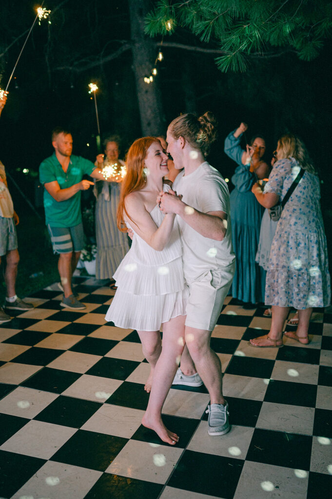 Bride and groom dancing on a checkered dance floor under sparklers. 