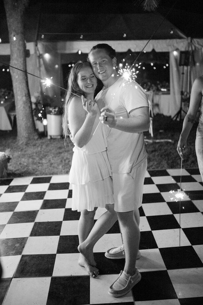 Bride and groom holding sparklers at the end of their reception on a checkered dance floor. 