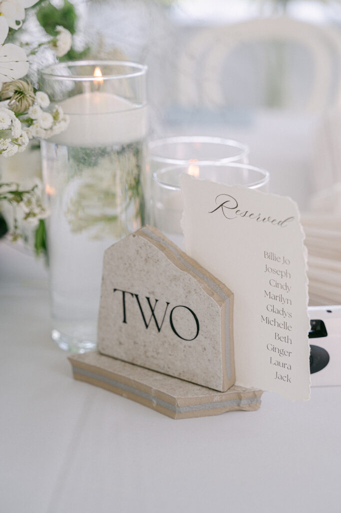 Stylish wedding reception with organic decor, including white linens and stone table numbers.