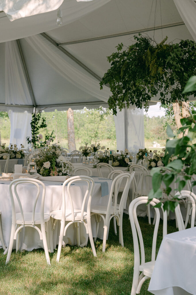 Charming tented reception with white linens, floral decor, and stone table numbers at a garden party wedding in Battle Lake. 