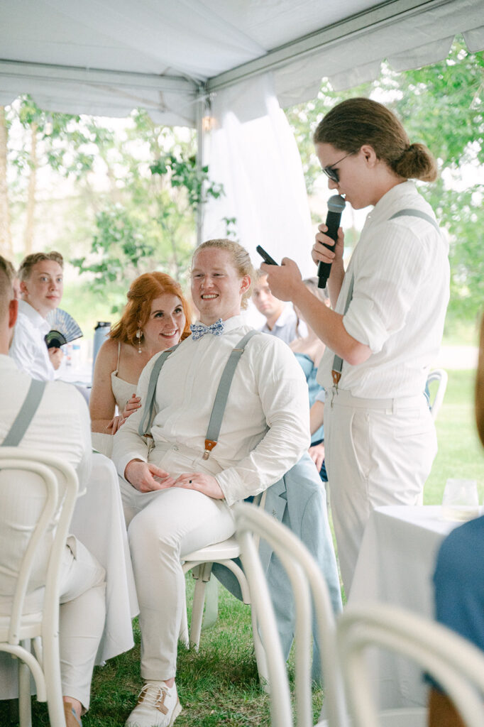 Bride and groom listening to emotional toasts from friends and family at their wedding dinner.