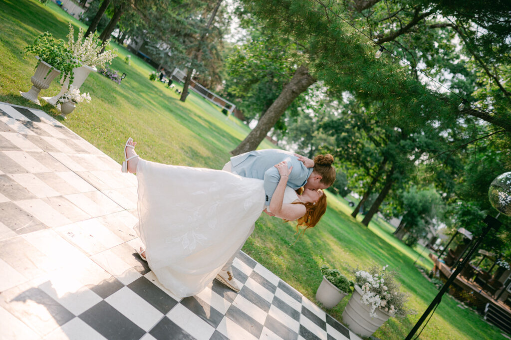 Intimate candid shot of the bride and groom first dance dip kiss on a checkered dance floor. 