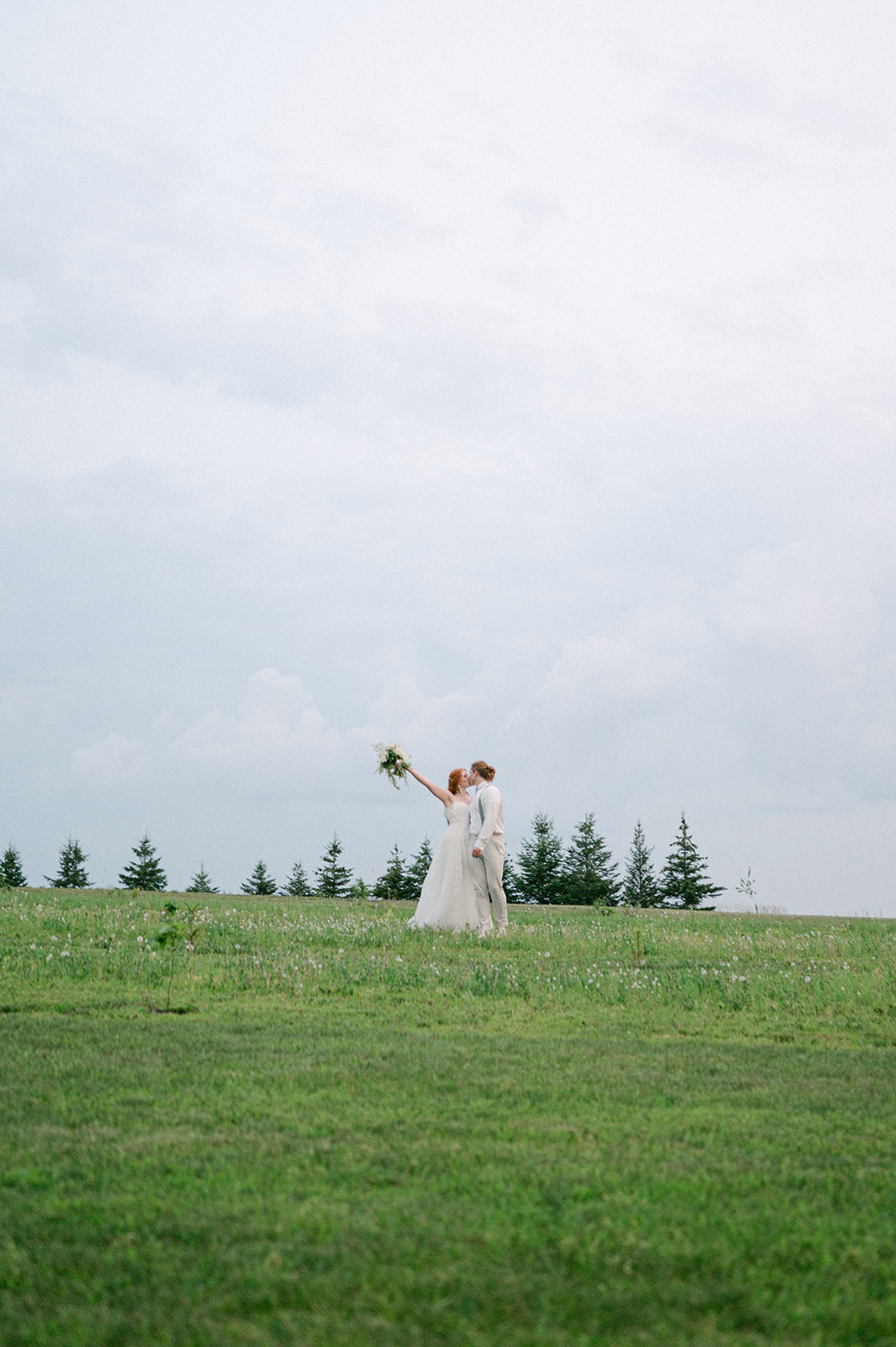 Documentary-style portrait of the bride and groom kissing in an open field at sunset in Battle Lake. 