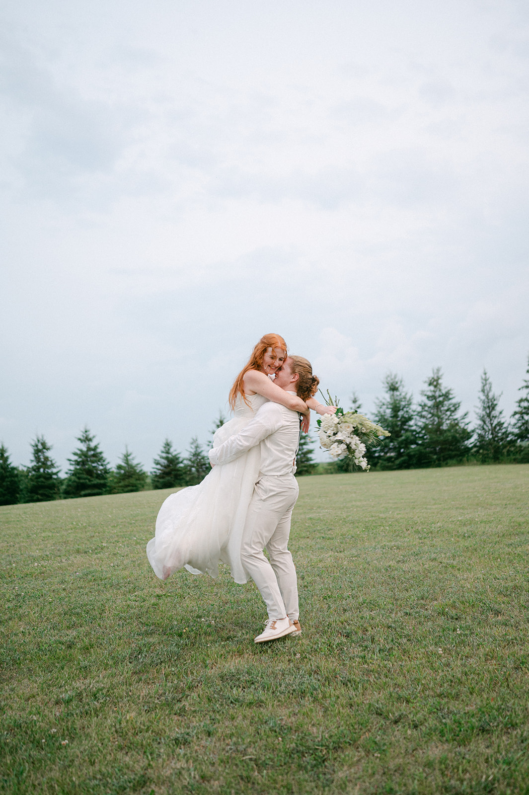 Playful documentary-style photo of the bride and groom embracing in a field field.