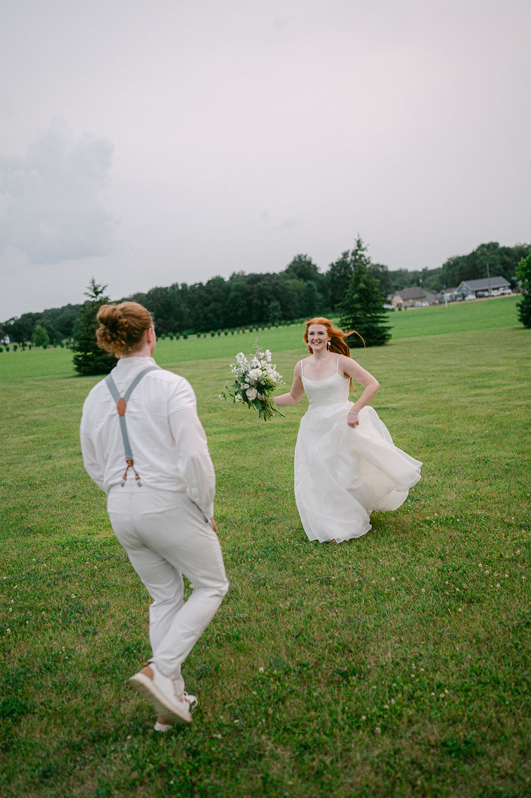 Cinematic portrait of the bride and groom running in a field, capturing their playful energy.