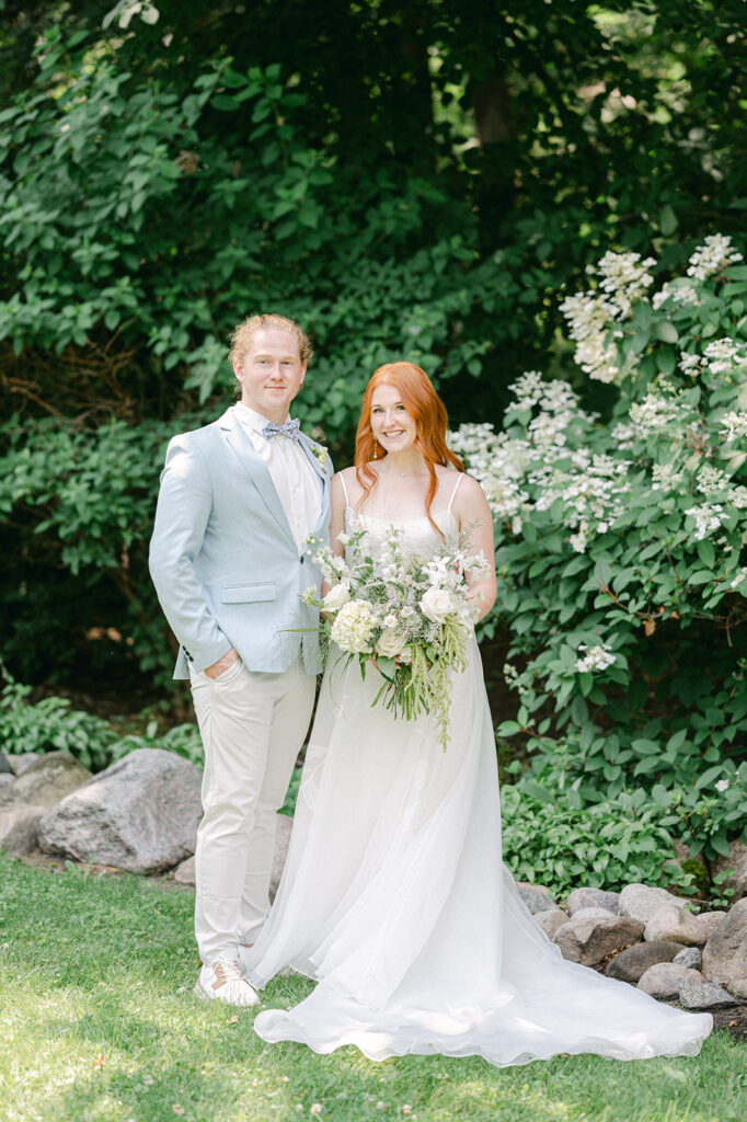 Elegant portrait of the newlyweds in the garden, the bride holding her white floral bouquet.