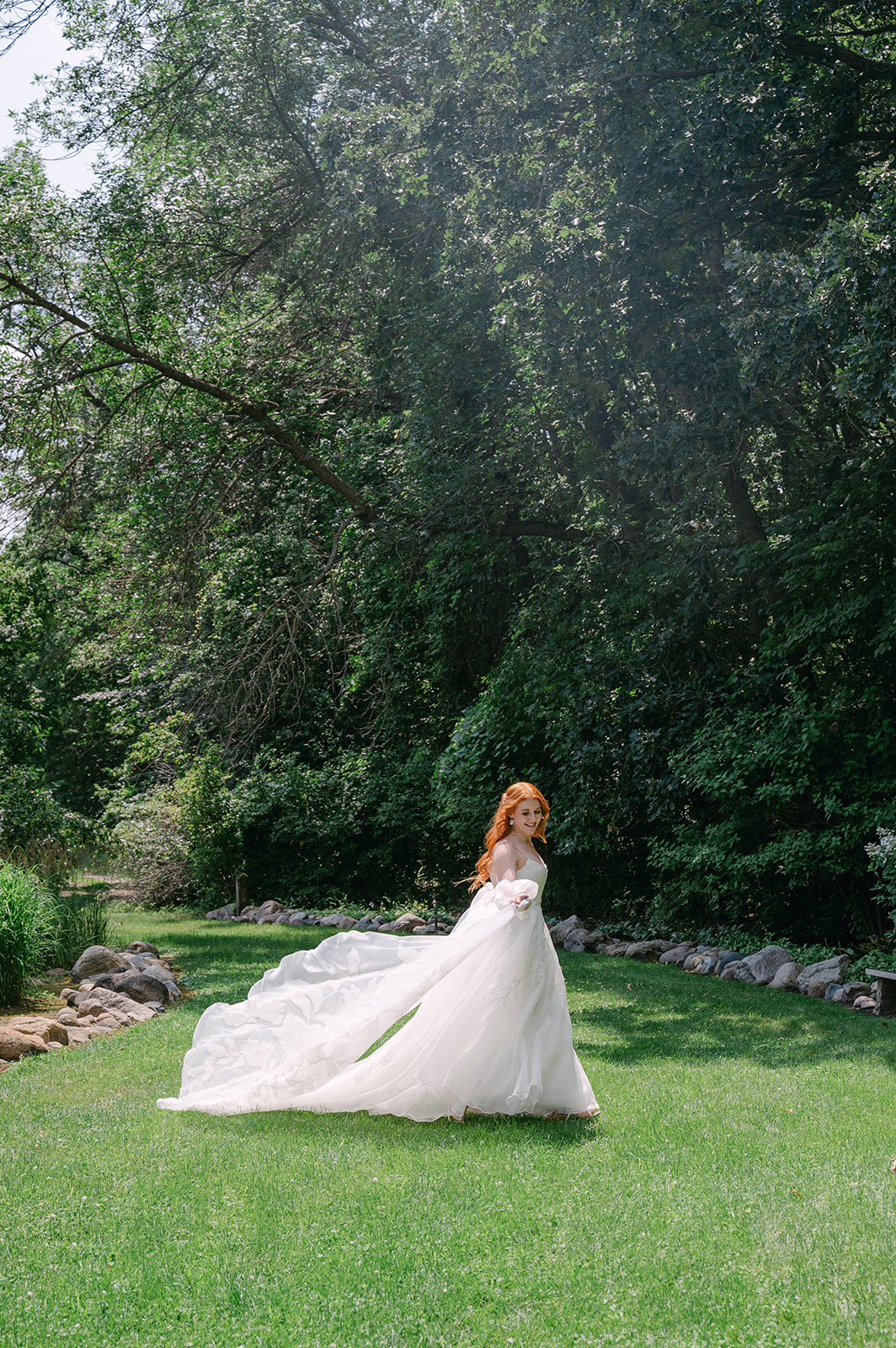 Whimsical bridal shot featuring a long, flowing dress set against the lush backdrop of her garden wedding at Battle Lake, MN.