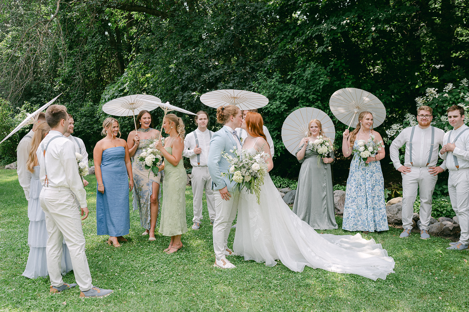 Unposed whimsical garden wedding party with mismatched floral bridesmaid dresses and paper parasol umbrellas.  