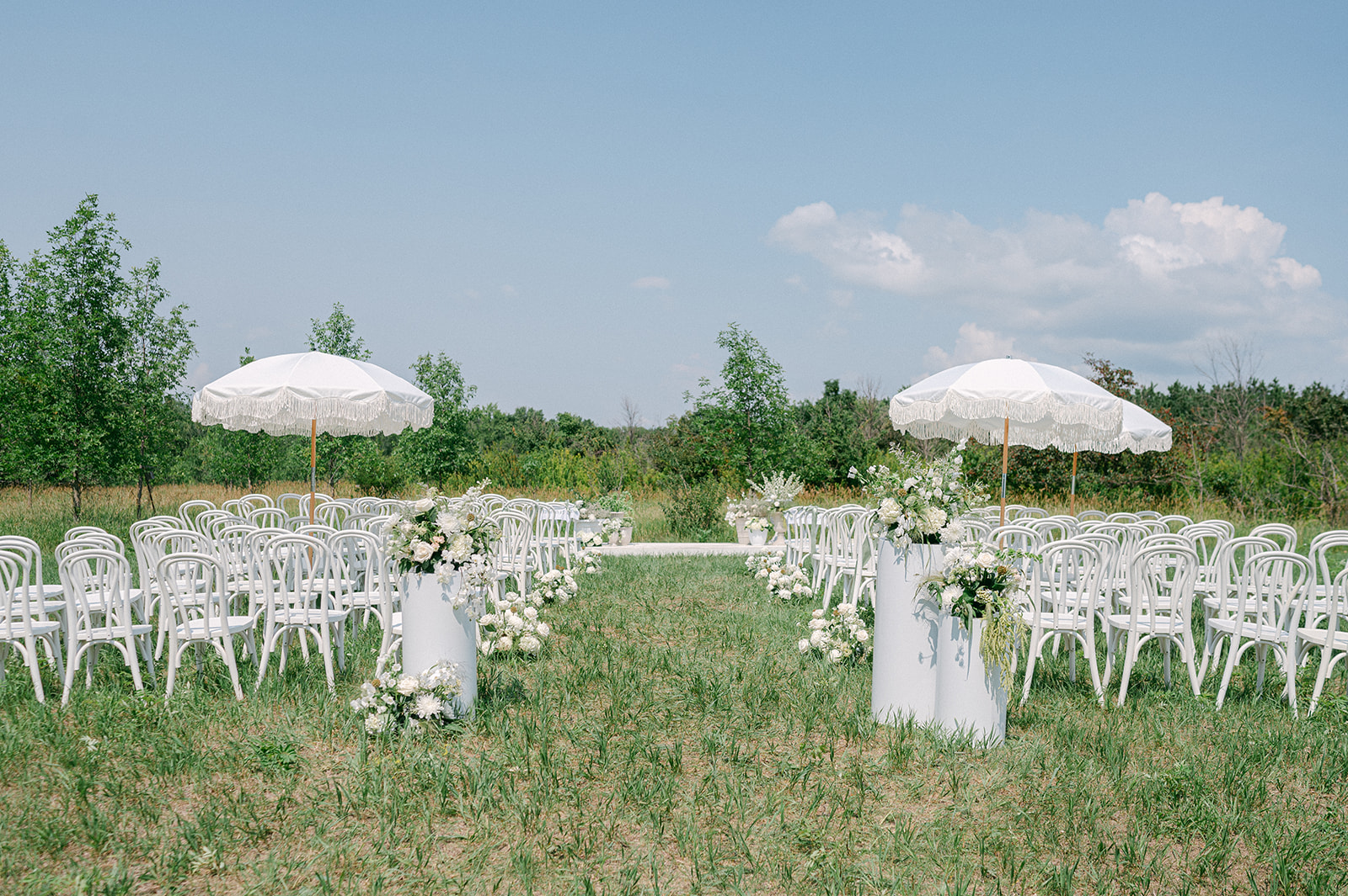 Open field outdoor wedding ceremony at Battle Lake, Minnesota with elegant white chairs and florals. 