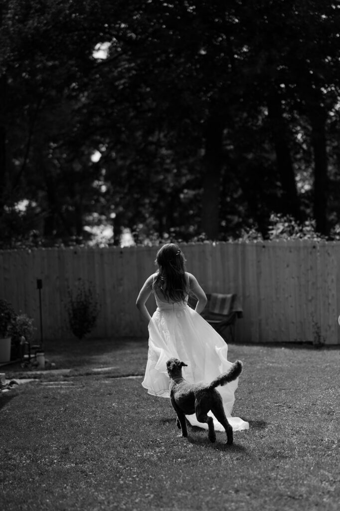 Black and white documentary style portrait of the bride playfully running with her dog at cocktail hour. 