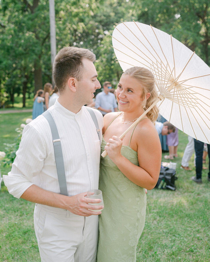 Bridesmaid holding a parasol umbrella smiling at her boyfriend at cocktail hour. 