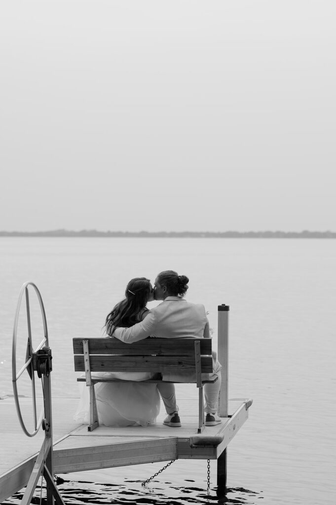 Bride and groom kissing on a bench overlooking Battle Lake at sunset. 