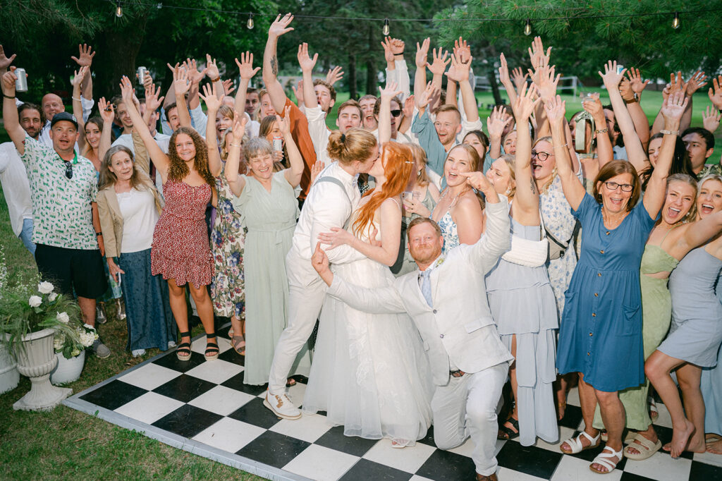 Direct flash bride and groom kissing with their entire wedding party holding up their hands in celebration. 