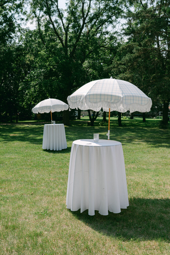 Summer garden party wedding cocktail tables with white linens and umbrellas. 