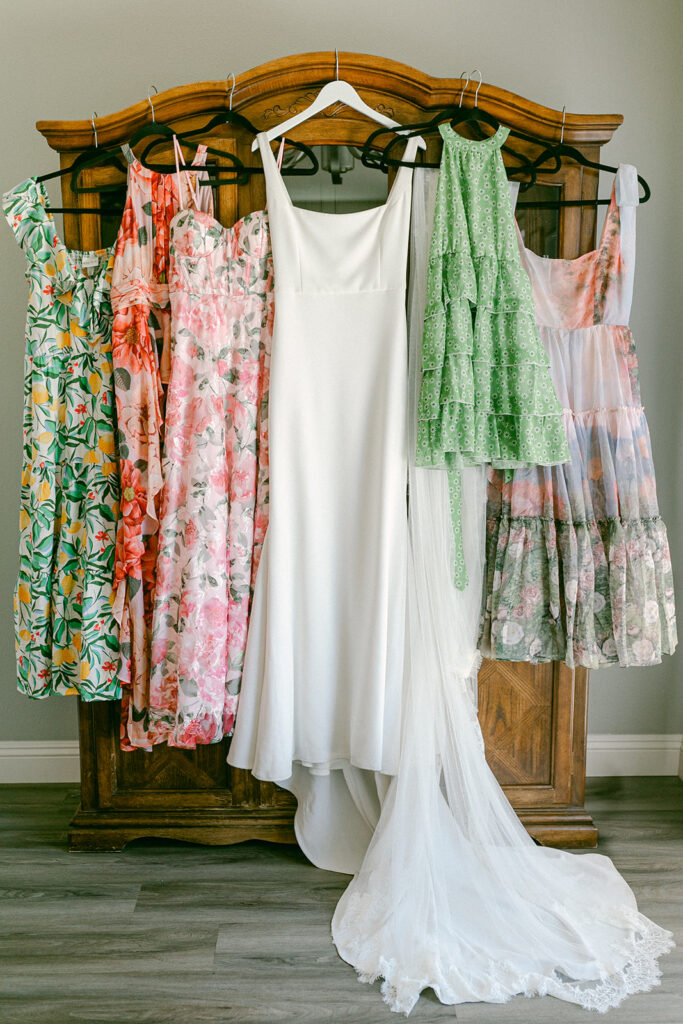 Wedding dress hanging photo with mismatched floral bridesmaid dresses. 