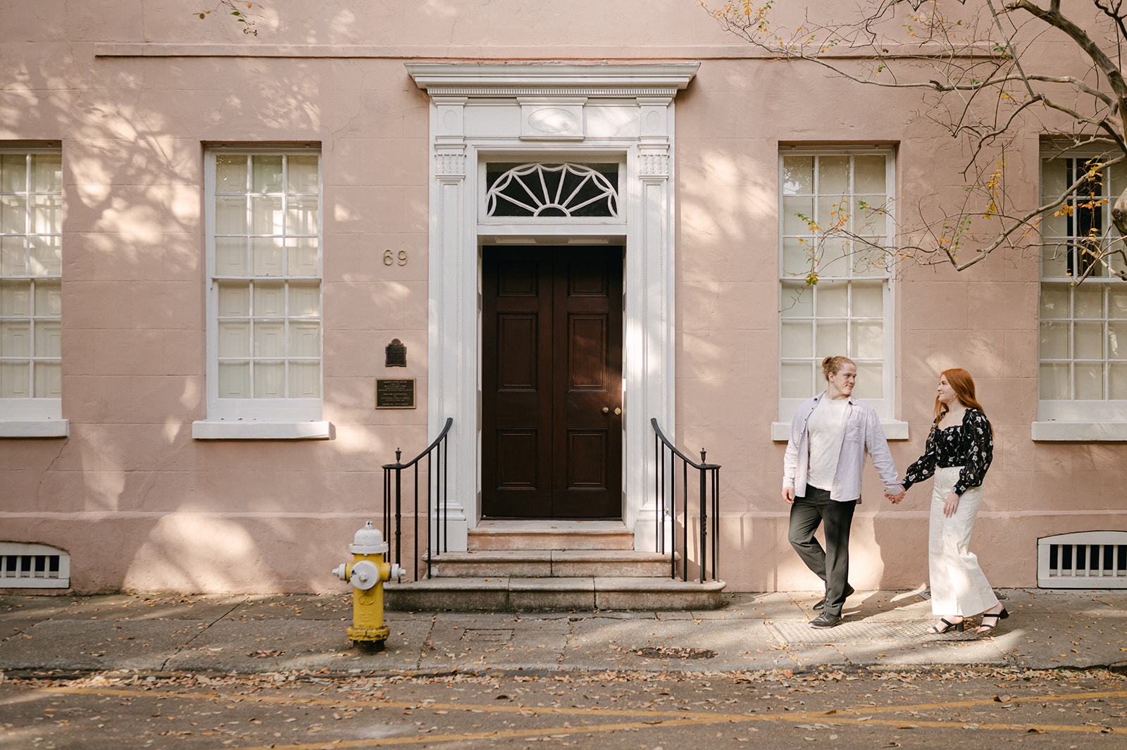 Couple walking in downtown Charleston with a pastel pink building in the background. 