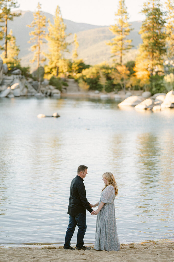 Couple hold hands on beach at Sand Harbor, a Lake Tahoe Engagement Photo Location.