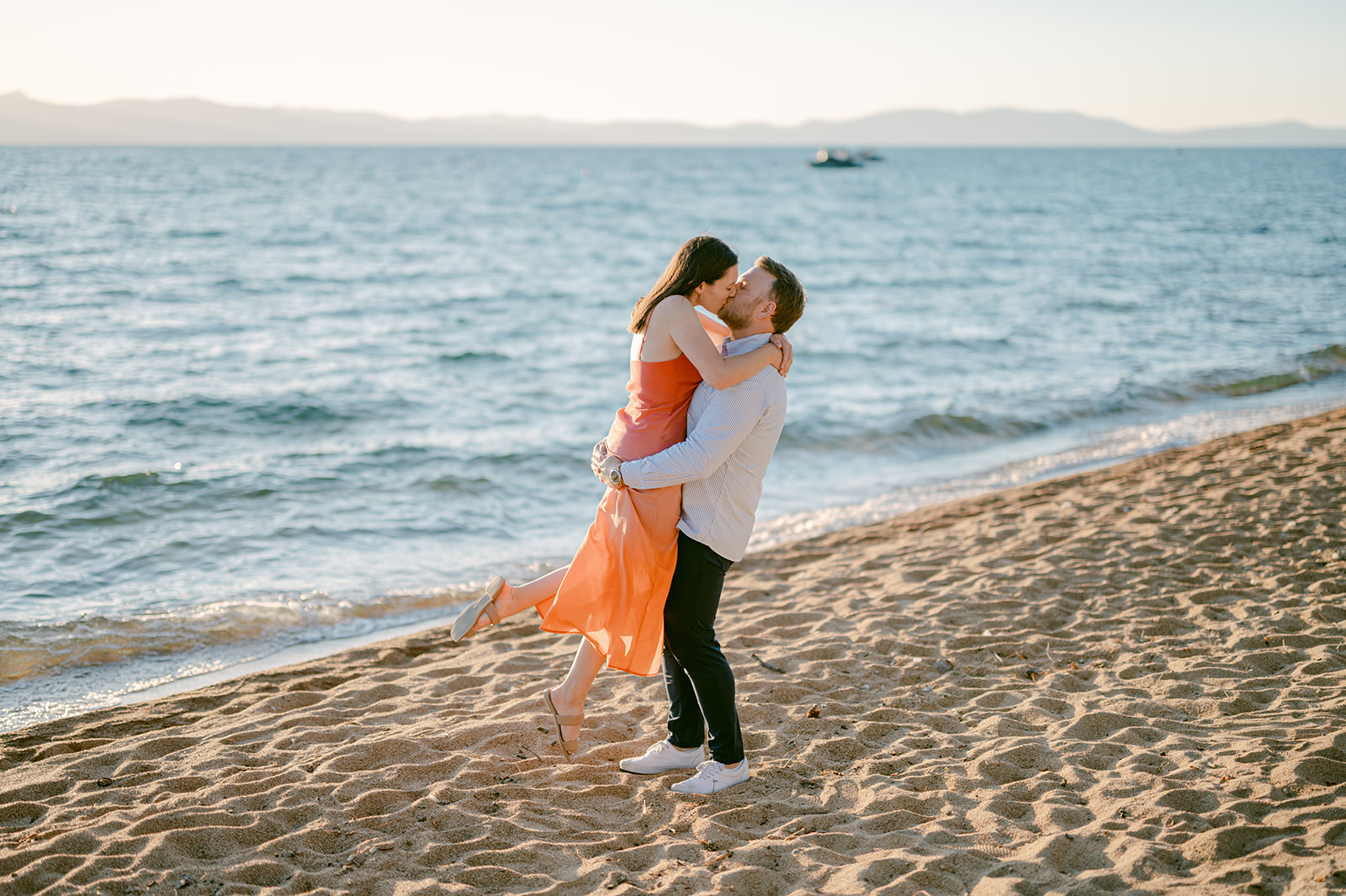 Man lifts his fiancé on Edgewood Resort beach in Lake Tahoe after engagement proposal.