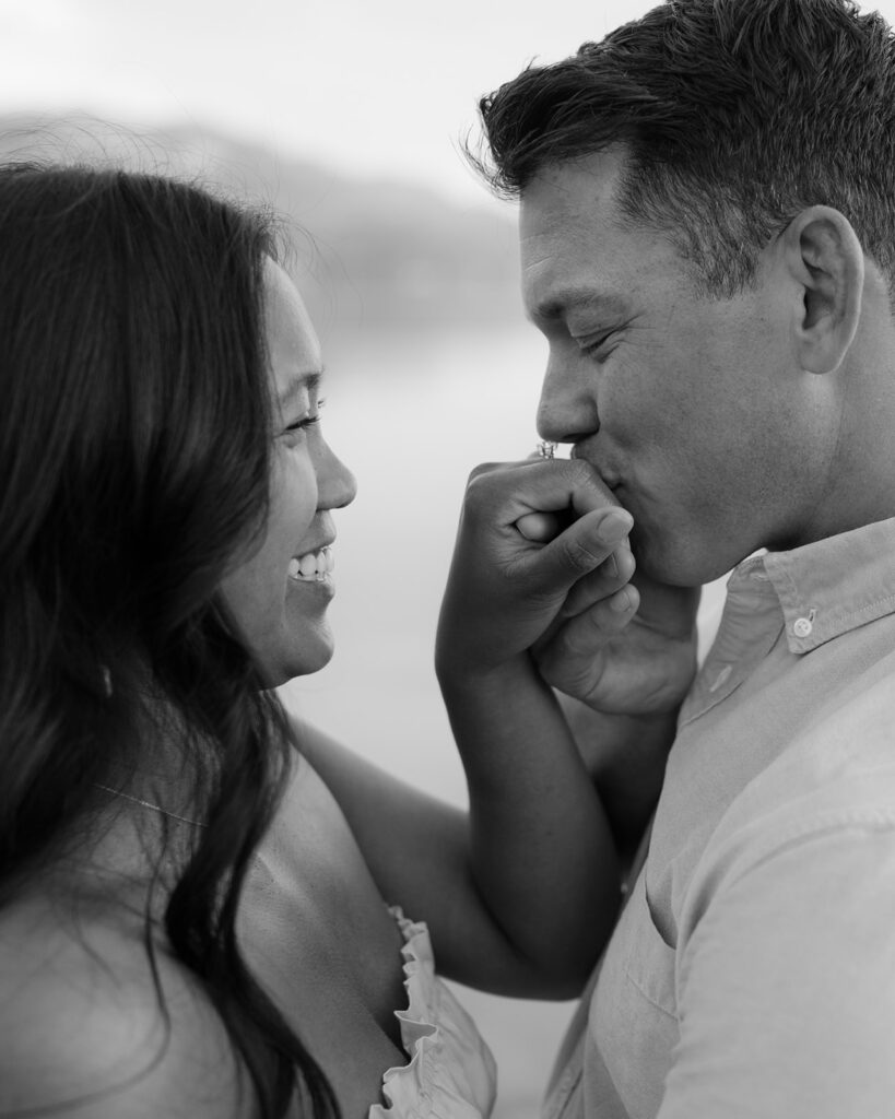 Man kissing is new fiancé's hand after proposing on the shore of Lake Tahoe.
