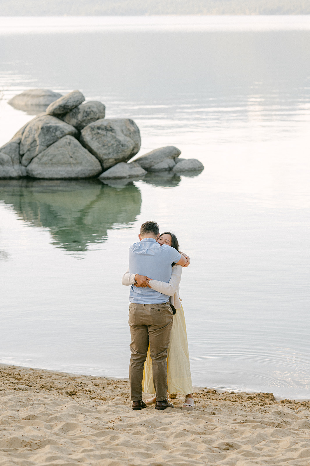 Couple hugging after their lakefront beach proposal.