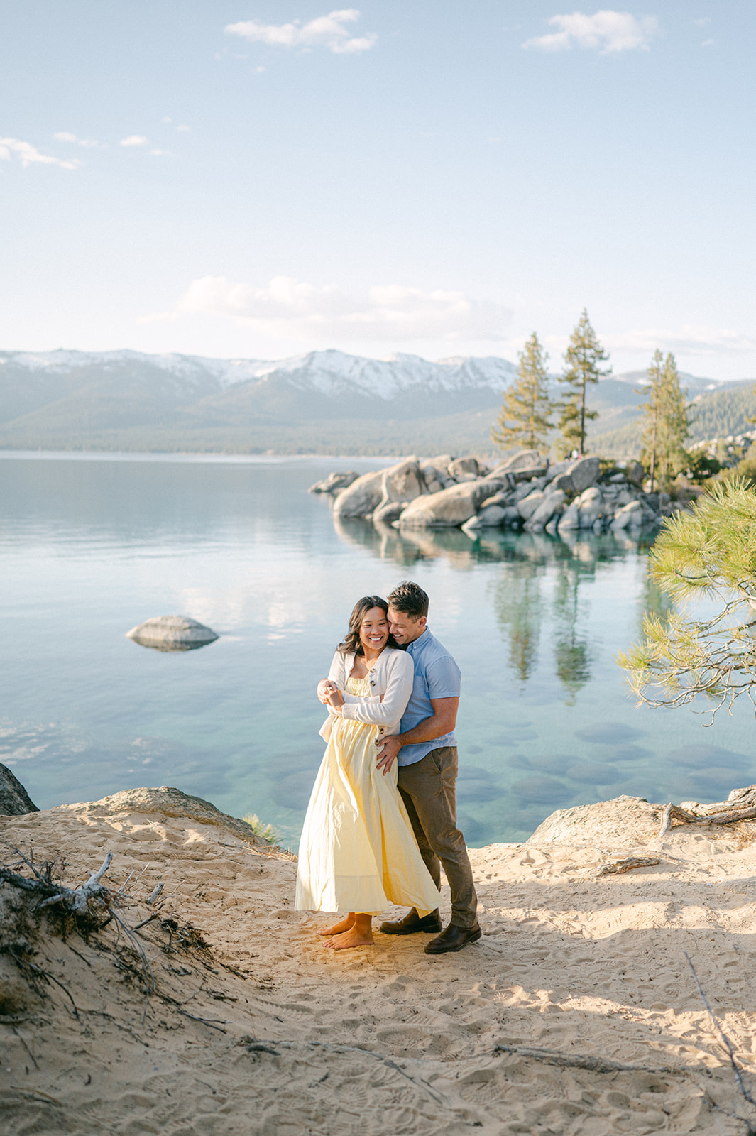 Couple embracing on the beach after their engagement with Lake Tahoe and mountains in the background.