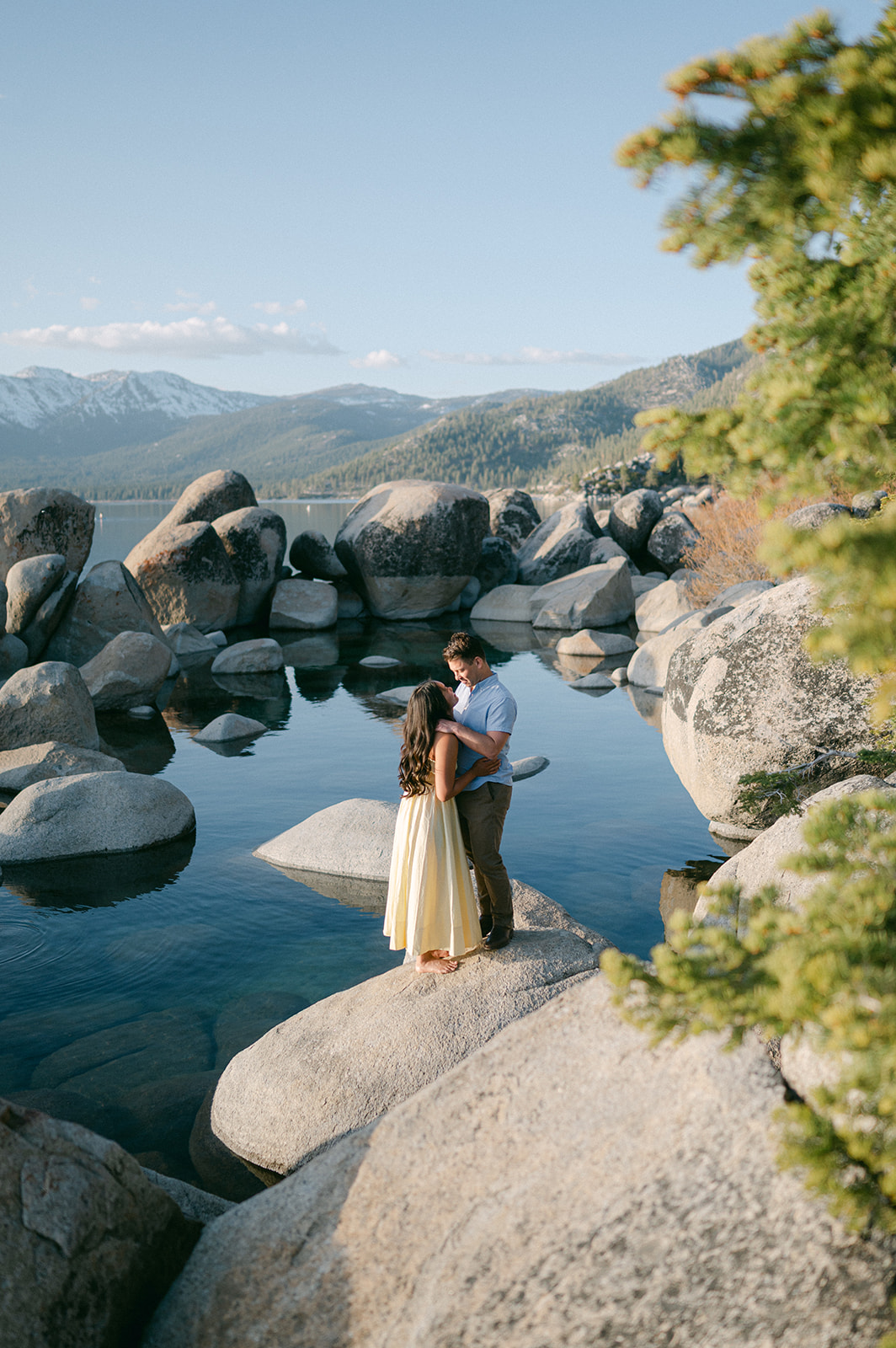 Couple leaning in for a kiss on the rocks at Sand Harbor with the lake in the background.