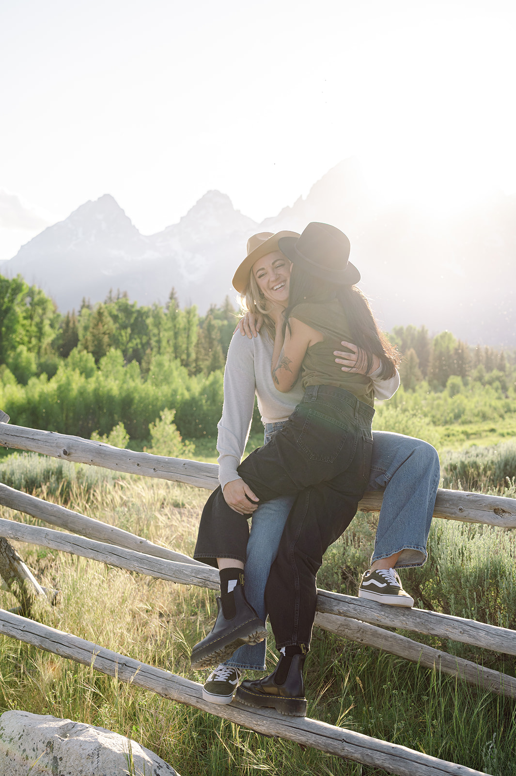 Cinematic anniversary photo in Jackson Hole featuring couple in cowboy hats sitting on a wooden fence
