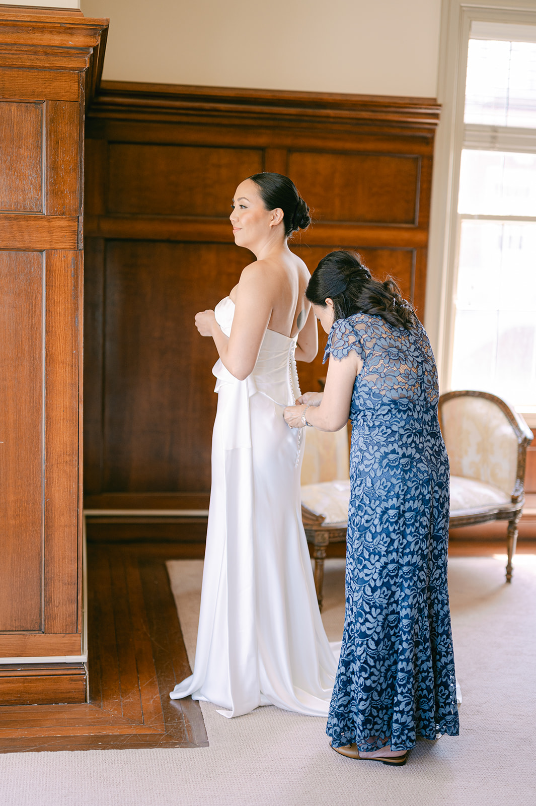 Mother helping bride button her gown before ceremony at Bay Area wedding.