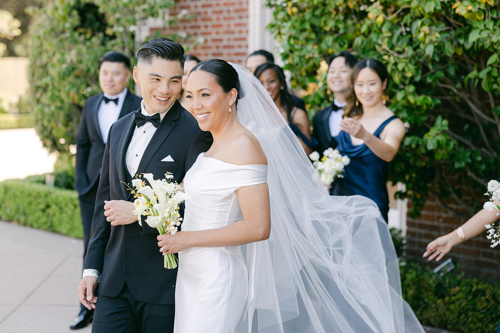 Bride and groom with wedding party gathered in front of Kohl Mansion, relaxed and candid.