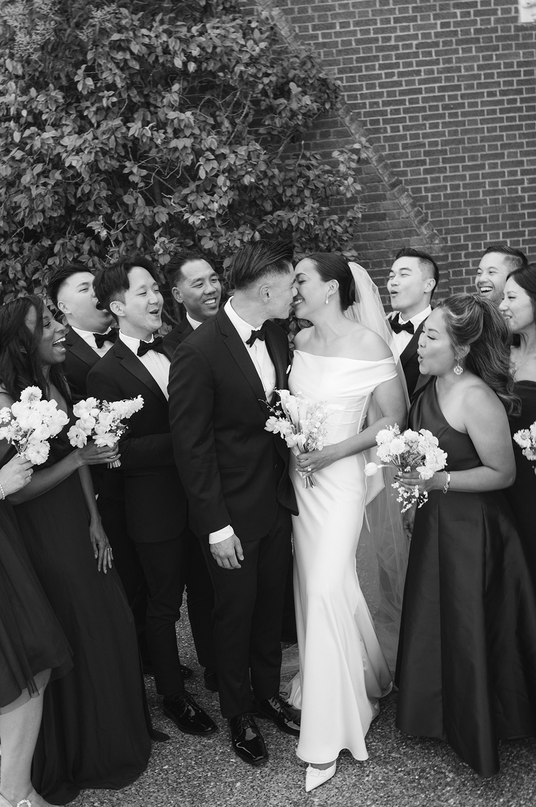 Documentary style wedding party group photo with couple kissing.