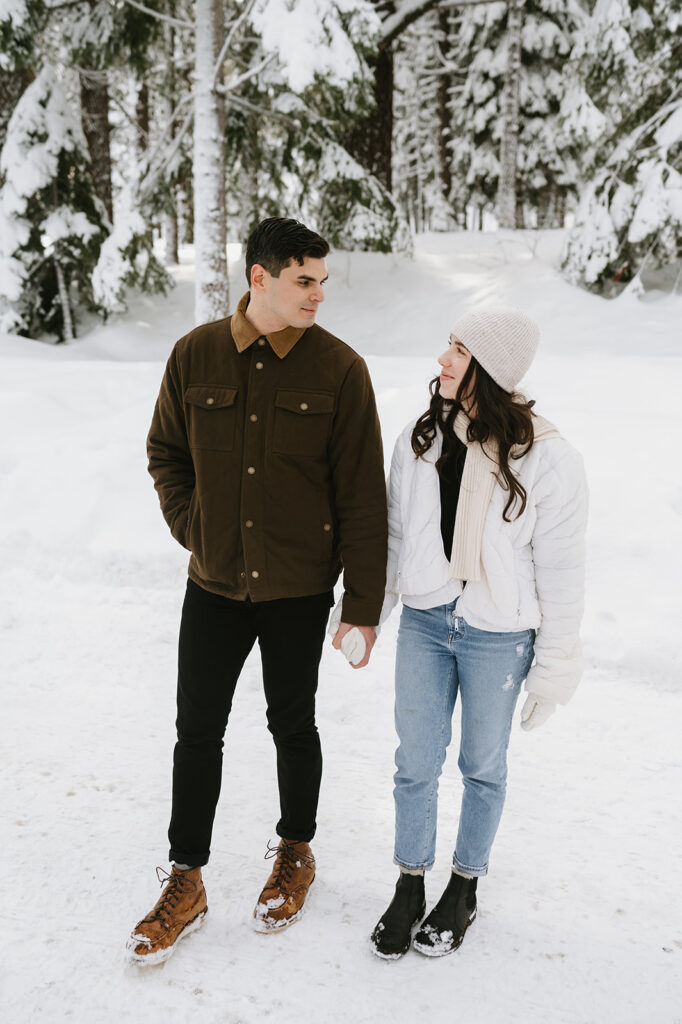 Couple wearing casual, layered winter outfits for their engagement photos in the snow. 