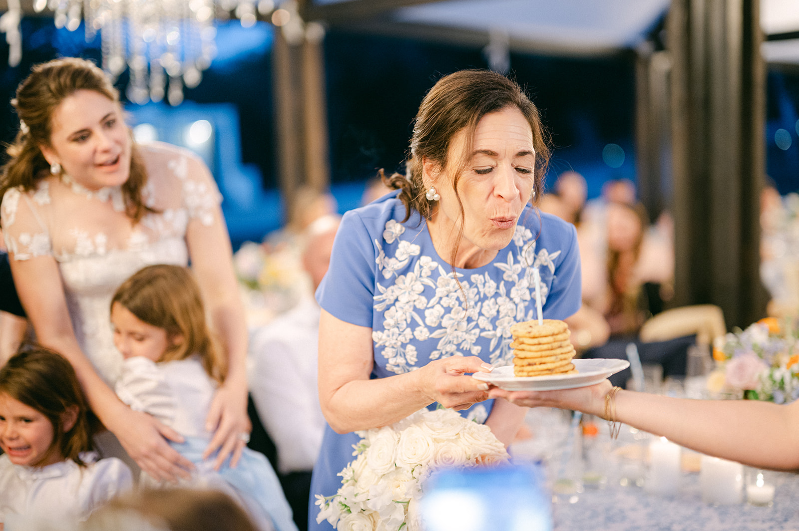 Bride's mom blowing out a birthday candle in a stack of cookies during their wedding reception.