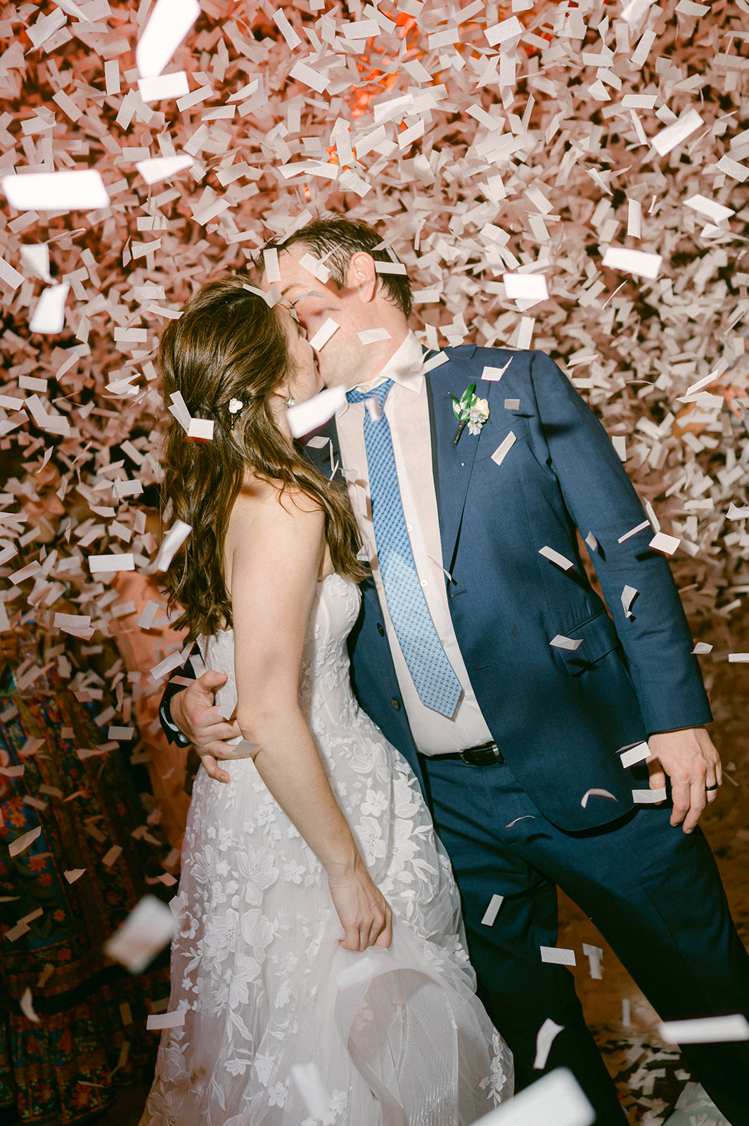 Bride and groom kissing under confetti during during Napa vineyard wedding reception.