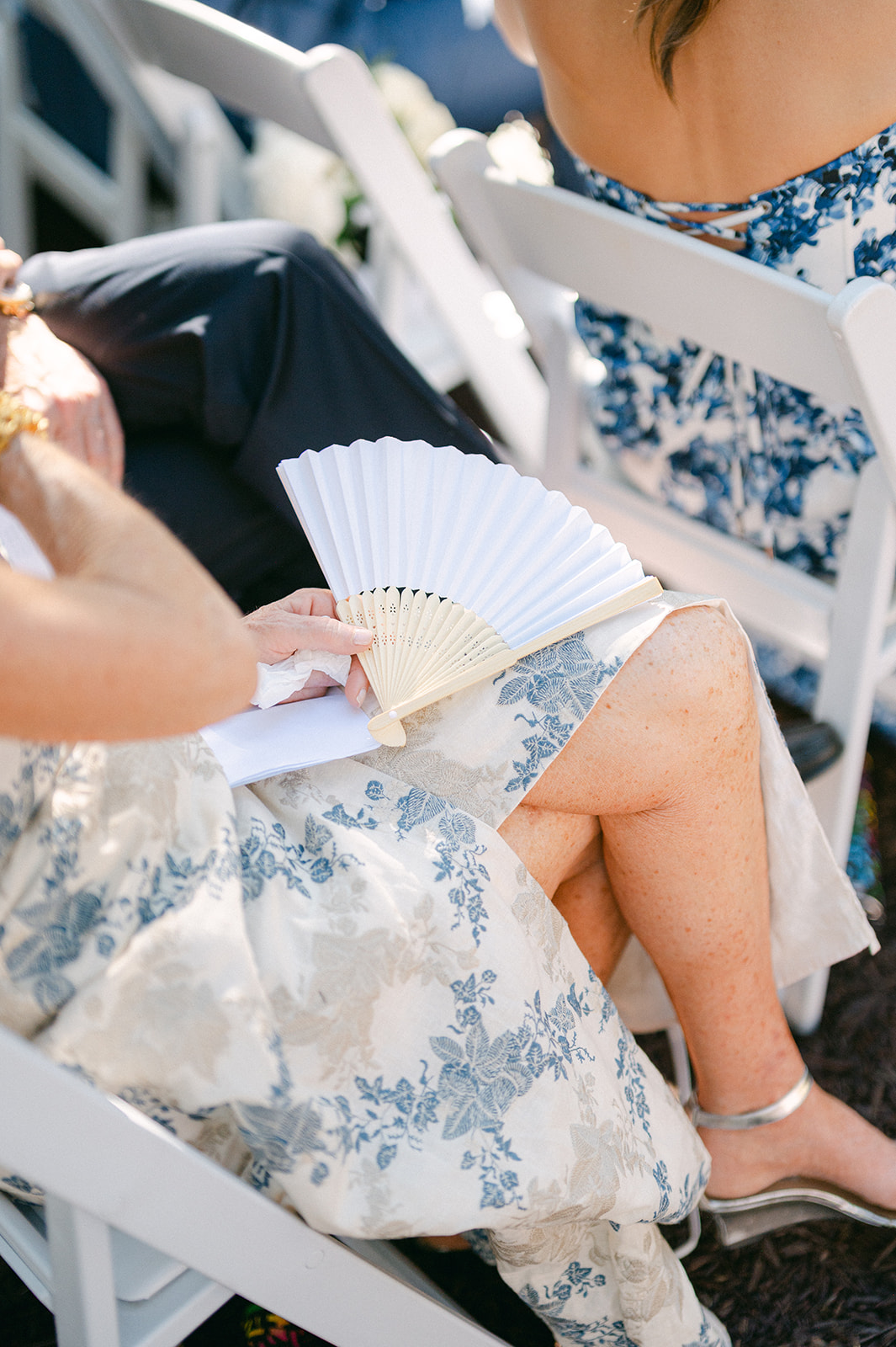 Guest holding paper fan during a hot vineyard wedding in Napa.