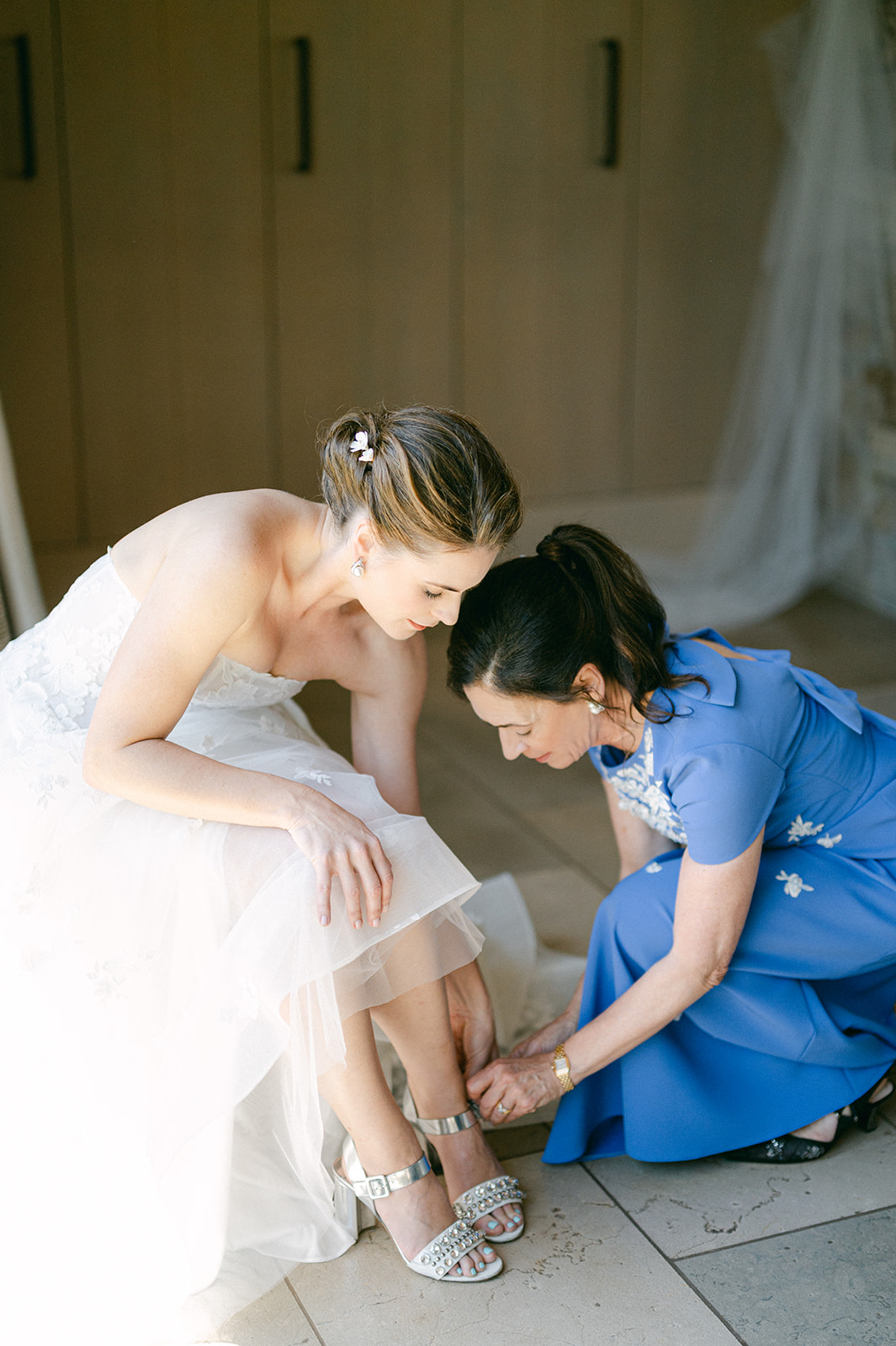 Bride's mom helping her put on her shoes. 