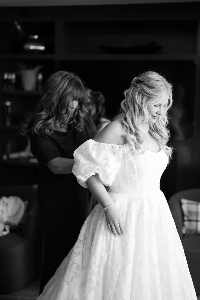 Bride getting her dress zipped up by her mom.