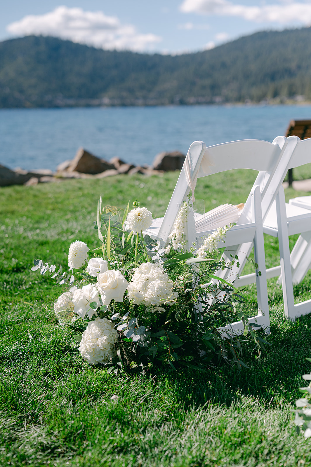 Lakeside wedding ceremony with white florals lining the aisle.