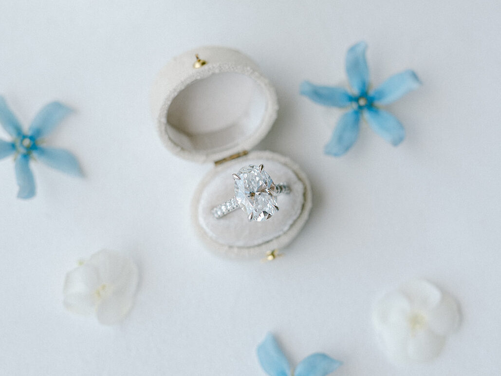 Oval engagement ring displayed in a white ring box surrounded by blue and white florals.