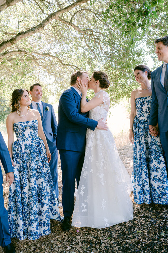 Bride and Groom kiss while surrounded by their wedding party at a Napa vineyard.