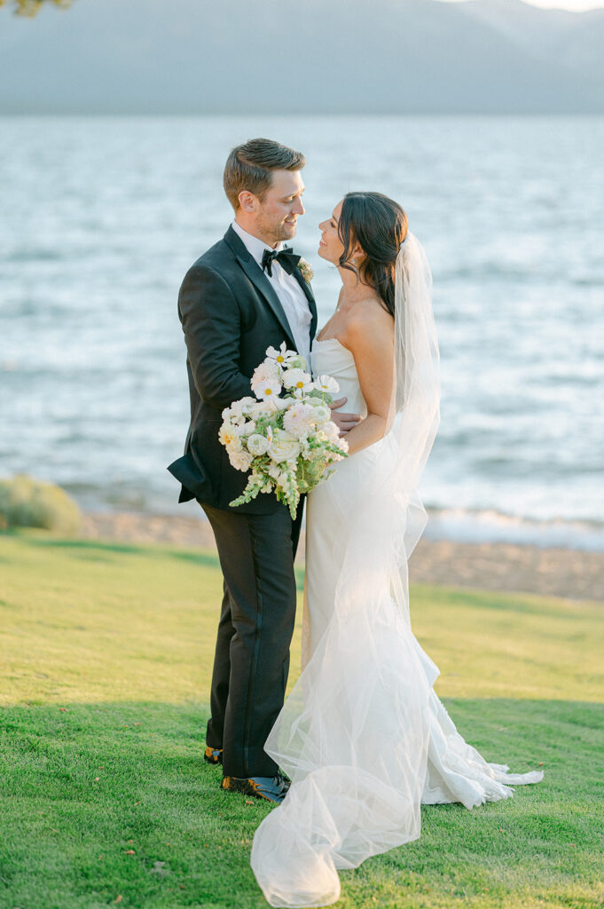 Newlyweds smile at each other while standing on the shore of Lake Tahoe.